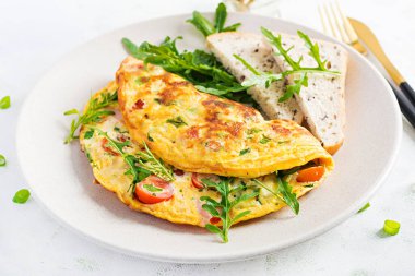Domatesli omlet, jambon, peynir ve tabakta yeşil otlar. Frittata - İtalyan omleti.