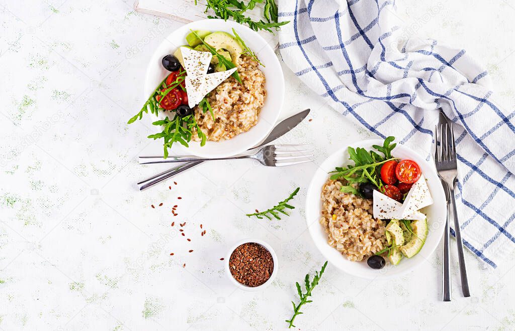 Breakfast oatmeal porridge with greek salad of tomatoes, avocado, black olives and arugula. Healthy balanced food. Top view, flat lay, copy space
