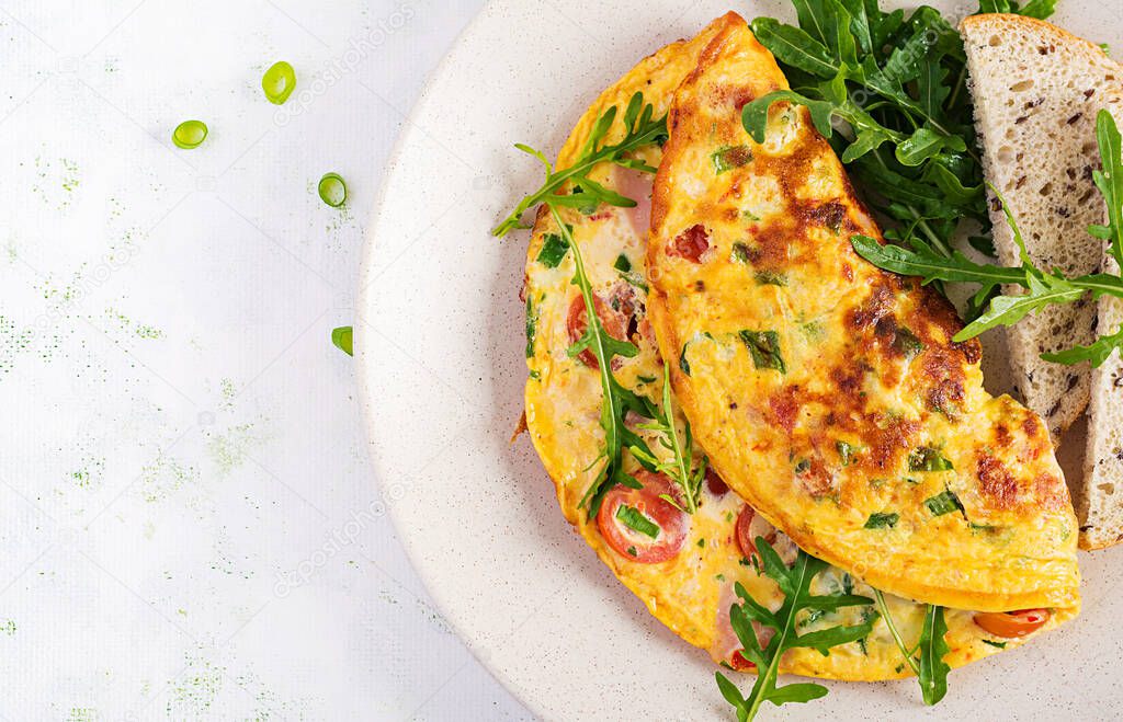 Omelette with tomatoes, ham, cheese and green herbs on plate.  Frittata - italian omelet. Top view, overhead, copy space