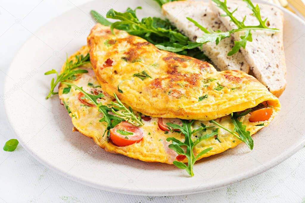 Omelette with tomatoes, ham, cheese and green herbs on plate.  Frittata - italian omelet.