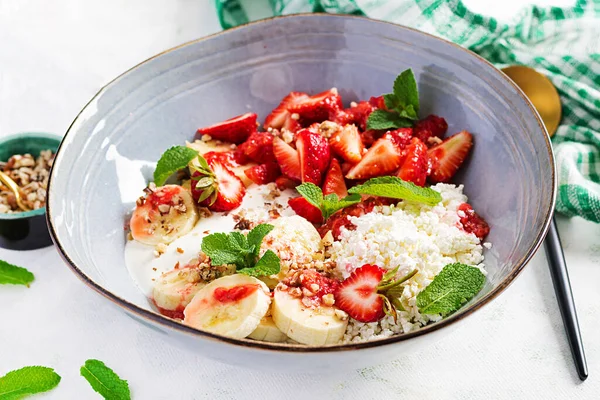 Cottage cheese or curd cheese with strawberries, bananas, walnuts in a blue bowl. Healthy food.