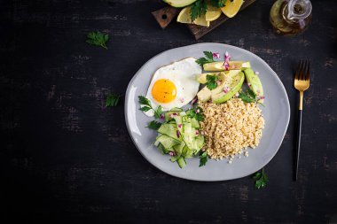 Diyet menüsü. Sağlıklı bir yaşam tarzı. Bulgur lapası, kızarmış yumurta ve taze sebzeler. Tabakta salatalık ve avokado. Üst görünüm, genel görünüm, kopyalama alanı