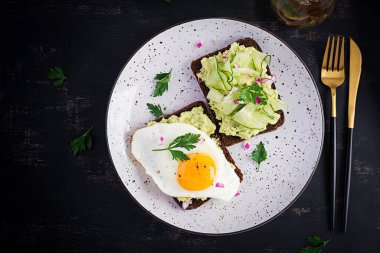 Sağlıklı kahvaltı. Avokado guacamole soslu sandviç, salatalık ve sahanda yumurta, sağlıklı kahvaltı veya atıştırmalık için. Üst görünüm, genel görünüm, düz görünüm