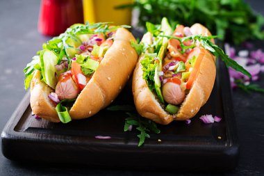 Sosisli sandviç, salatalık, domates ve koyu arkaplanda kırmızı soğan..