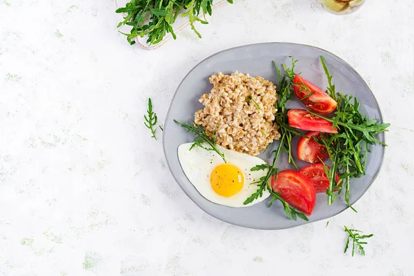 Kahvaltı yulaf lapası, sahanda yumurta, domates ve roka. Sağlıklı yiyecekler. Üst görünüm, genel görünüm, kopyalama alanı