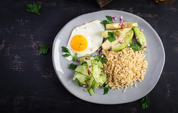 Diet menu. Healthy lifestyle. Bulgur porridge, fried egg and fresh vegetables -  cucumber and avocado on plate. Top view, overhead, copy space