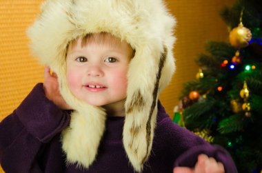 İki yıl eski güzel bir Noel ağacı yakınındaki beyaz, Rus, Kürk şapkalı küçük kız portresi. rahat ışık