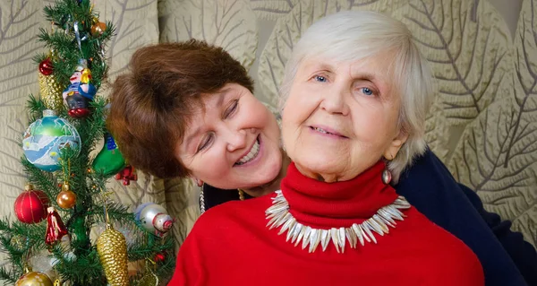 Family moments at Christmas time. old woman smile. grandmother and her daughter are sitting near Christmas tree. spirit of New Year. background is a rich interior. hug each other