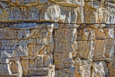 Taş duvar gibi, katmanlı ve çatlak beyaz kaya güneş ışığında, mavi gölgeler ile.