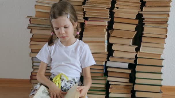 小さな女の子が床に座って本をページング — ストック動画
