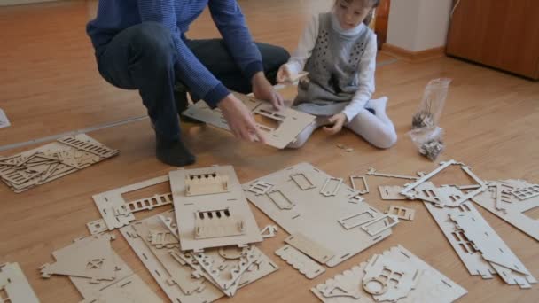 Маленька дівчинка з батьком будує дерев'яний іграшковий будинок — стокове відео