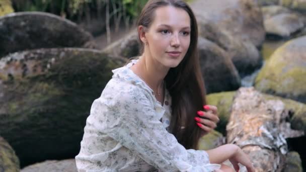 Mooi meisje zitten op steen in bos — Stockvideo