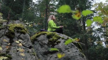 Ormandaki bir kayanın üzerinde meditasyon yapan kadın.