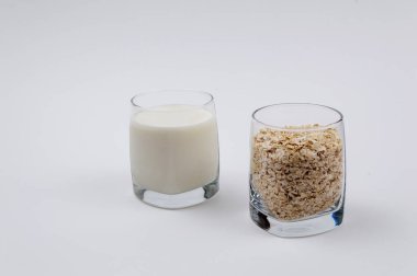 Bir bardak süt ve bir bardak yulaf gevreği beyaz bir arka plan üzerinde dolu dolu