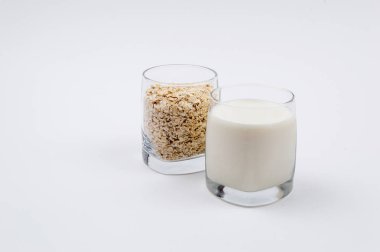 Bir bardak süt ve bir bardak yulaf gevreği beyaz bir arka plan üzerinde dolu dolu