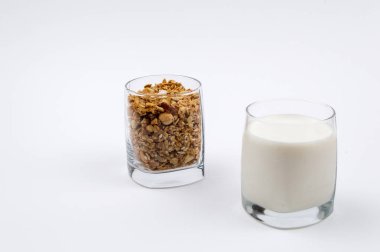 Bir bardak süt ve bir bardak beyaz zemin üzerine müsli dolu dolu