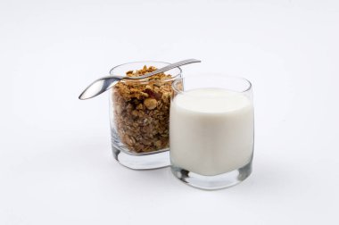 Bir bardak süt ve bir bardak beyaz zemin üzerinde bir paslanmaz çelik kaşık müsli tam dolu