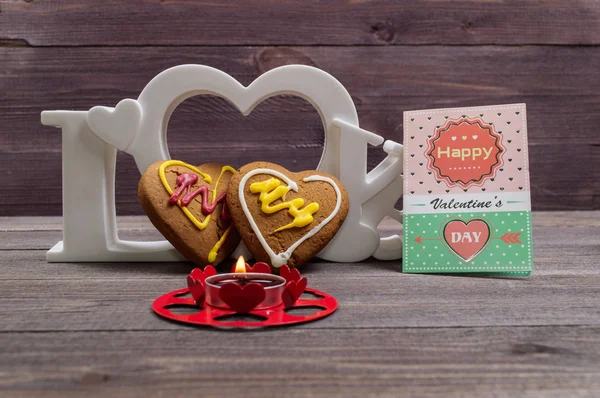 Two heart shaped cookies, a red candle and the word love on a wooden table on Valentine\'s Day