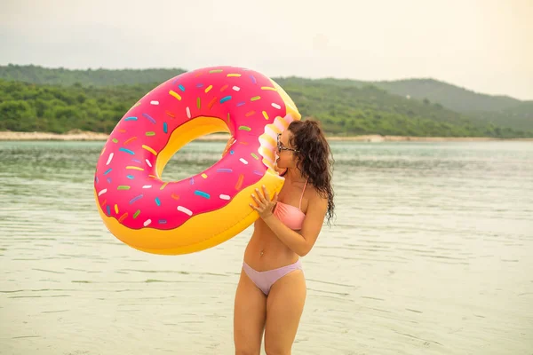 ビキニを着て砂浜でピンク膨らませてドーナツ マットレスを保持している女性 — ストック写真