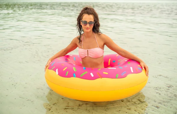 ビキニを着て砂浜でピンク膨らませてドーナツ マットレスを保持している女性 — ストック写真