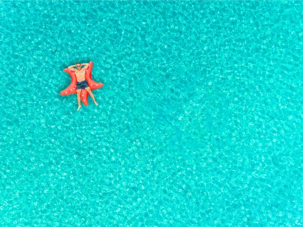 人漂浮在充气星鱼床垫上的鸟图 手臂交叉在透明的海面上 — 图库照片
