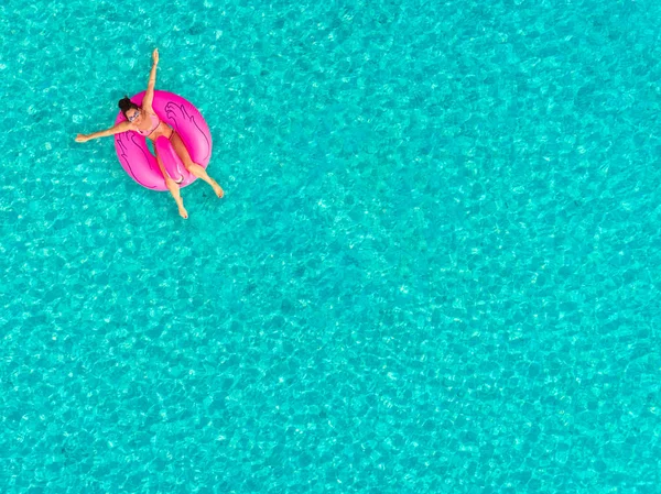 Aerial view of woman floating on inflatable donut shaped mattress, sunbathing.