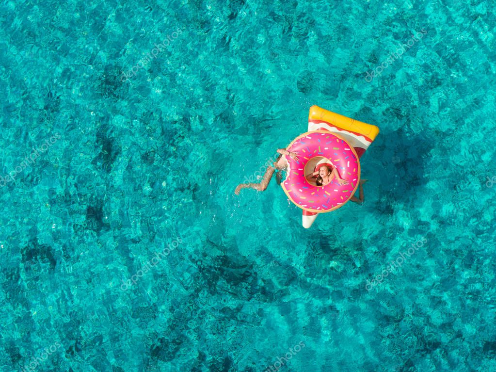 Aerial view of two young girls playing in sea on pizza and donut shaped inflatables.