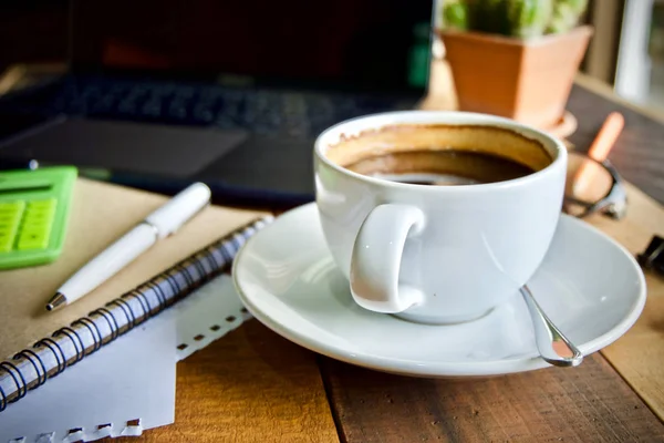 Kahve fincanı sıcak ve dizüstü defter kalem ahşap masa masa üzerinde