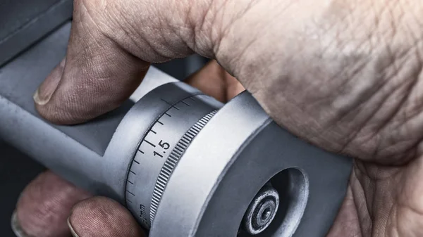 Control knob of machine tool in detail. Close-up of dirty hand on the metal wheel with a vernier scale for accurate measurement. Idea of precise machining in production and mechanical engineering.