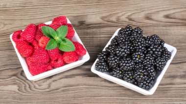 Taze ahududu ve böğürtlen Bahçe bir tablo. Beyaz tatlı sulu orman meyve nane ve ahşap arka plan dekoratif yeşil yaprakları ile kase kare. Biyo tatlı sağlıklı uzuvlar.