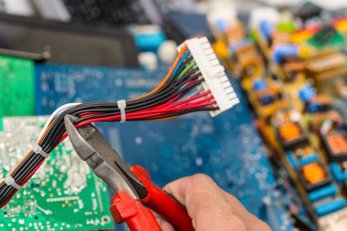 İşçinin elinde kerpetenle elektronik atık bertarafı. Bilgisayar anakart güç kabloları konektörle. Renkli devre kartları yığını. Elektrik demonte ve bilgisayar parçaları. Seçici odak.
