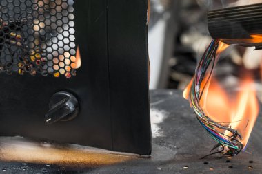 Alevler içindeki elektrik kabloları ve trafik veya endüstriyel kaza yüzünden mahvolmuş enkaz parçaları. Kırık enkazlarda elektrik kabloları ya da şalterli siyah metal kaplama ve altıgen ızgara. Terörizm, savaş.