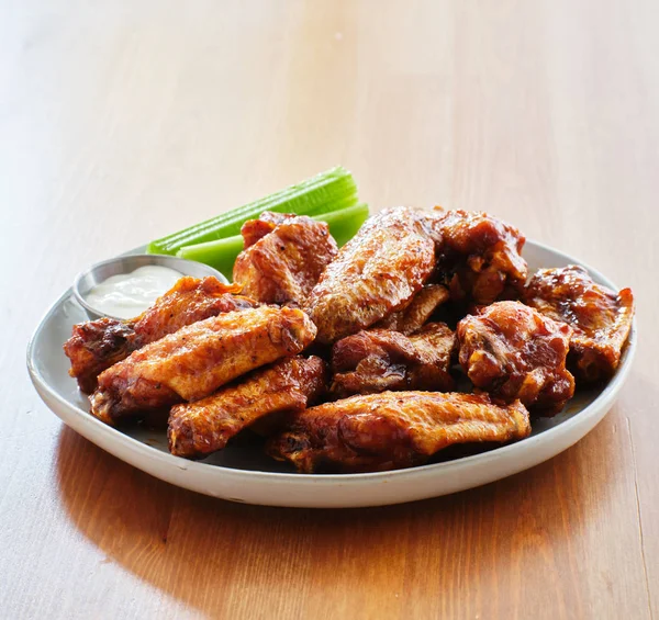 plate of bbq chicken wings with ranch dip and celery sticks on wooden table