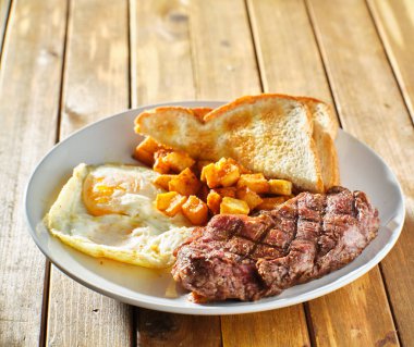 steak and eggs breakfast with toast and homestyle potatoes on wooden table clipart