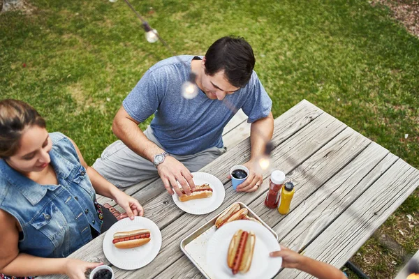 裏庭のピクニックテーブルで焼きホットドッグを食べる幸せなヒスパニック系の家族 — ストック写真