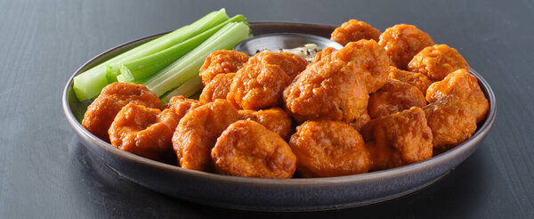 plate of boneless chicken wings with buffalo sauce and celery sticks