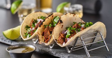Üç Meksika carne asada sokak tacosuyla metal taco tutacağı.
