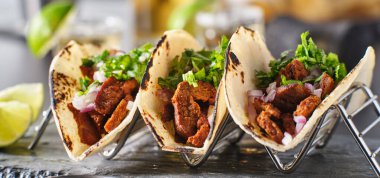 Üç Meksika carne asada sokak tacosuyla metal taco tutacağı.