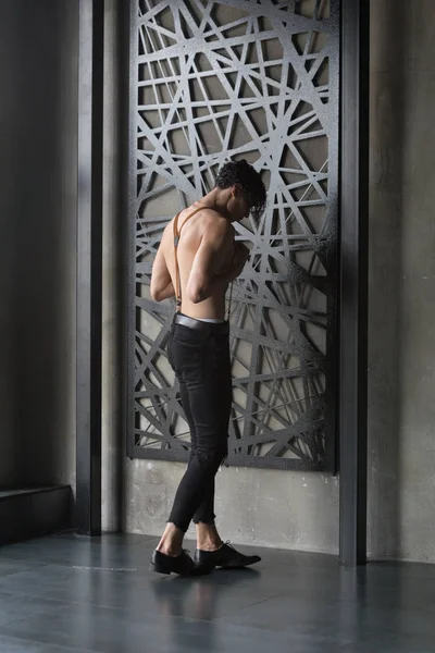 Yakışıklı gömleksiz koyu saçlı manken karanlık bir odada yırtık kot pantolon arkadan görünüş