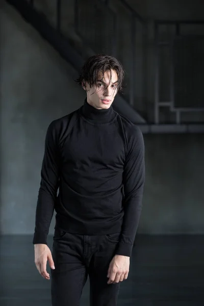 Islak siyah saçlı balıkçı yaka ile tüm siyah kıyafeti ve karanlık bir odada yırtık kot pantolon ile şık yakışıklı genç adam