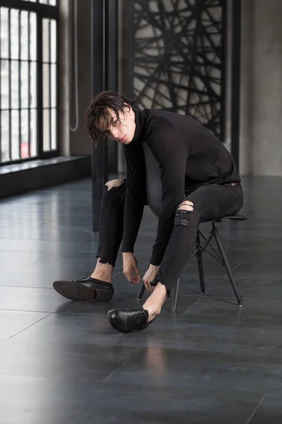 Şık yakışıklı delikanlı balıkçı yaka ve karanlık bir odada bir sandalyede oturan yırtık kot pantolon ile tüm siyah kıyafeti ıslak siyah saçlı