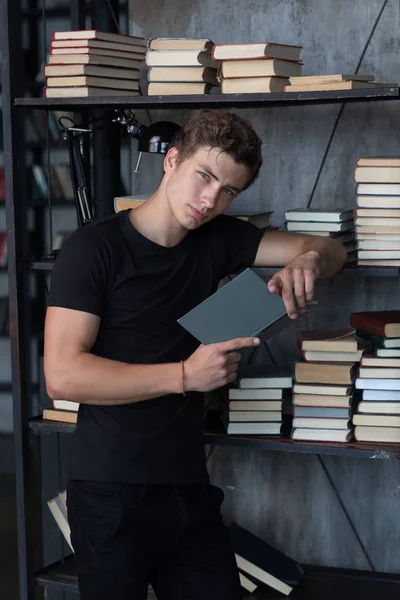 Yakışıklı genç erkek model bookshelve modern bir iç profesyonel photostudio, tüm siyah kıyafeti yakınındaki poz