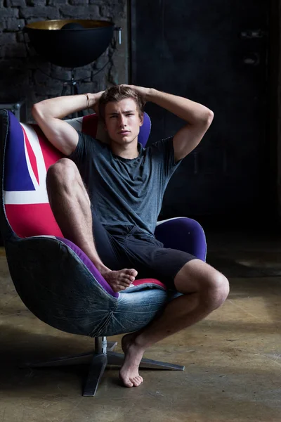 Profesyonel bir photostudio trendy hipster içinin gri gömlek ve siyah şort IAT bir sandalyede oturan kahverengi saçlı yakışıklı genç