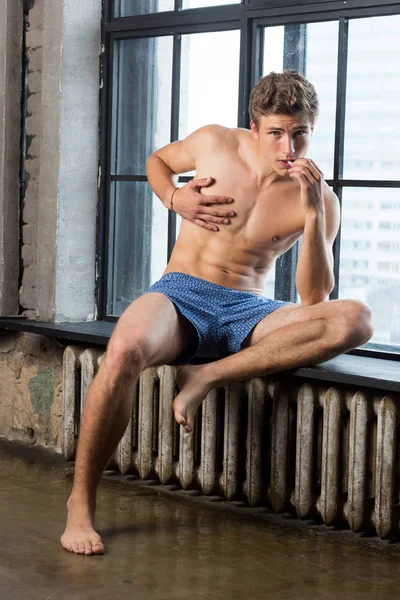 Yakışıklı brutall ama şirin Rus erkek model iç çamaşırı sigara bir pencere pervazına üzerinde oturan