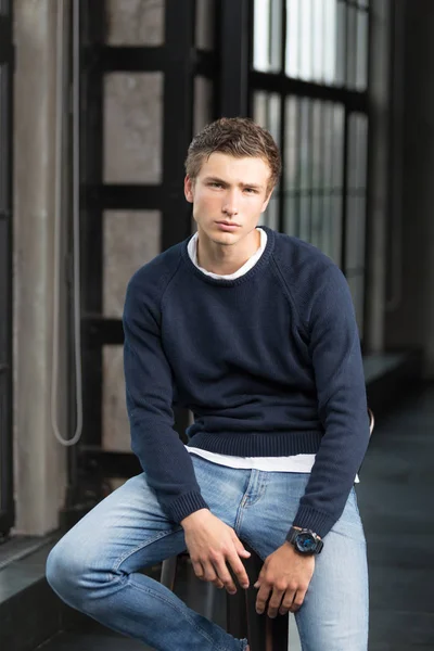 Handsome young male model in a blue sweater looking at camera at modern interior photostudio
