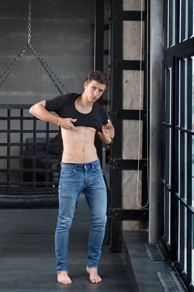 Full body portrait of a handsome young male model undressing showing off his abs at modern interior photostudio