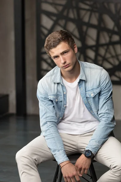 Handsome young male model in blue shirt and white pants at modern interior photostudio