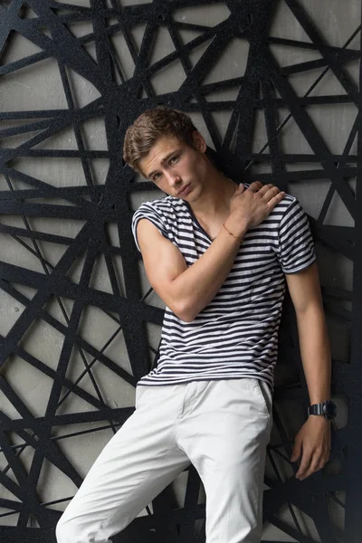 Handsome young male model in stripes t-shirt and white pants posing at modern interior photostudio