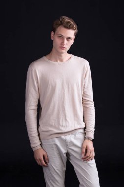 Yakışıklı erkek model mavi gözleri ve hafif curlie saç bej kazak ve karanlık bir arka plan üzerinde beyaz pantolon