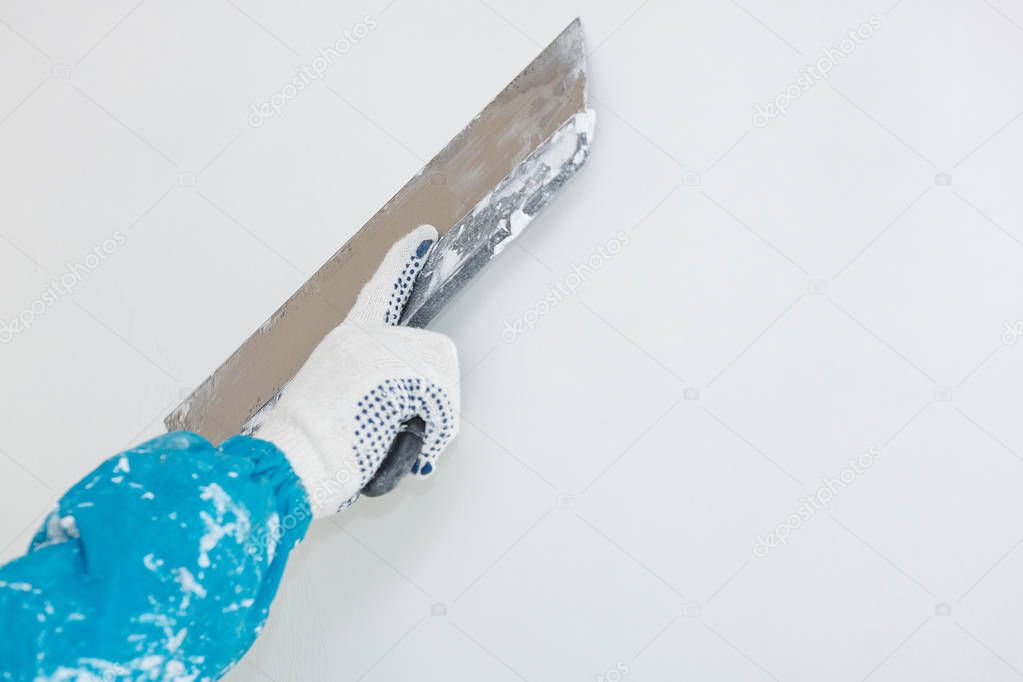 Hand with a spatula in the process of leveling the raw plaster.